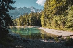 A mountain lake with clear green water, surrounded by trees. The distant mountains are covered with snow, the scenery is very beautiful. - free wallpaper image