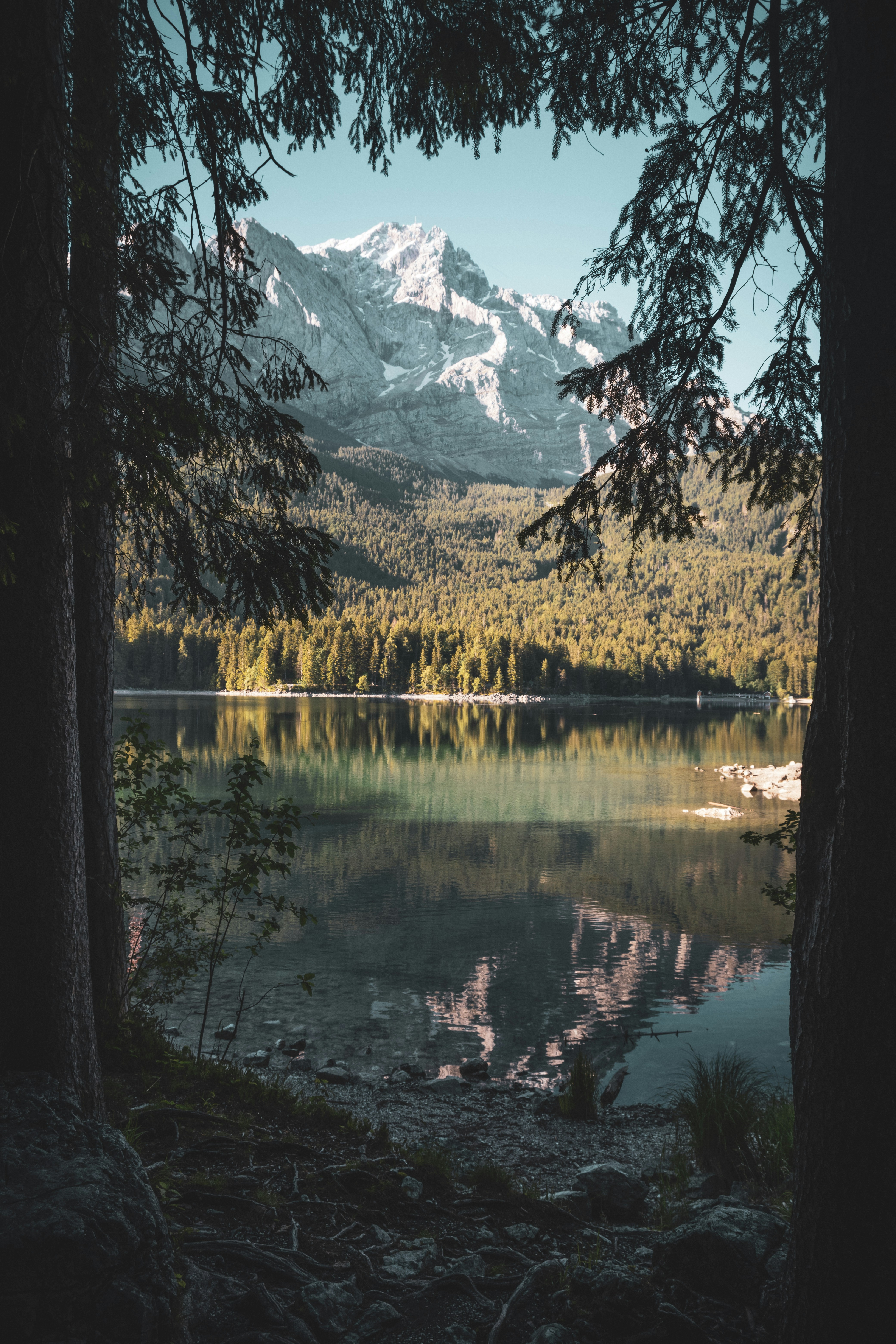 A mountain lake with clear water reflecting the snowy mountains and surrounding trees. The lake is surrounded by lush forests. - free wallpaper image