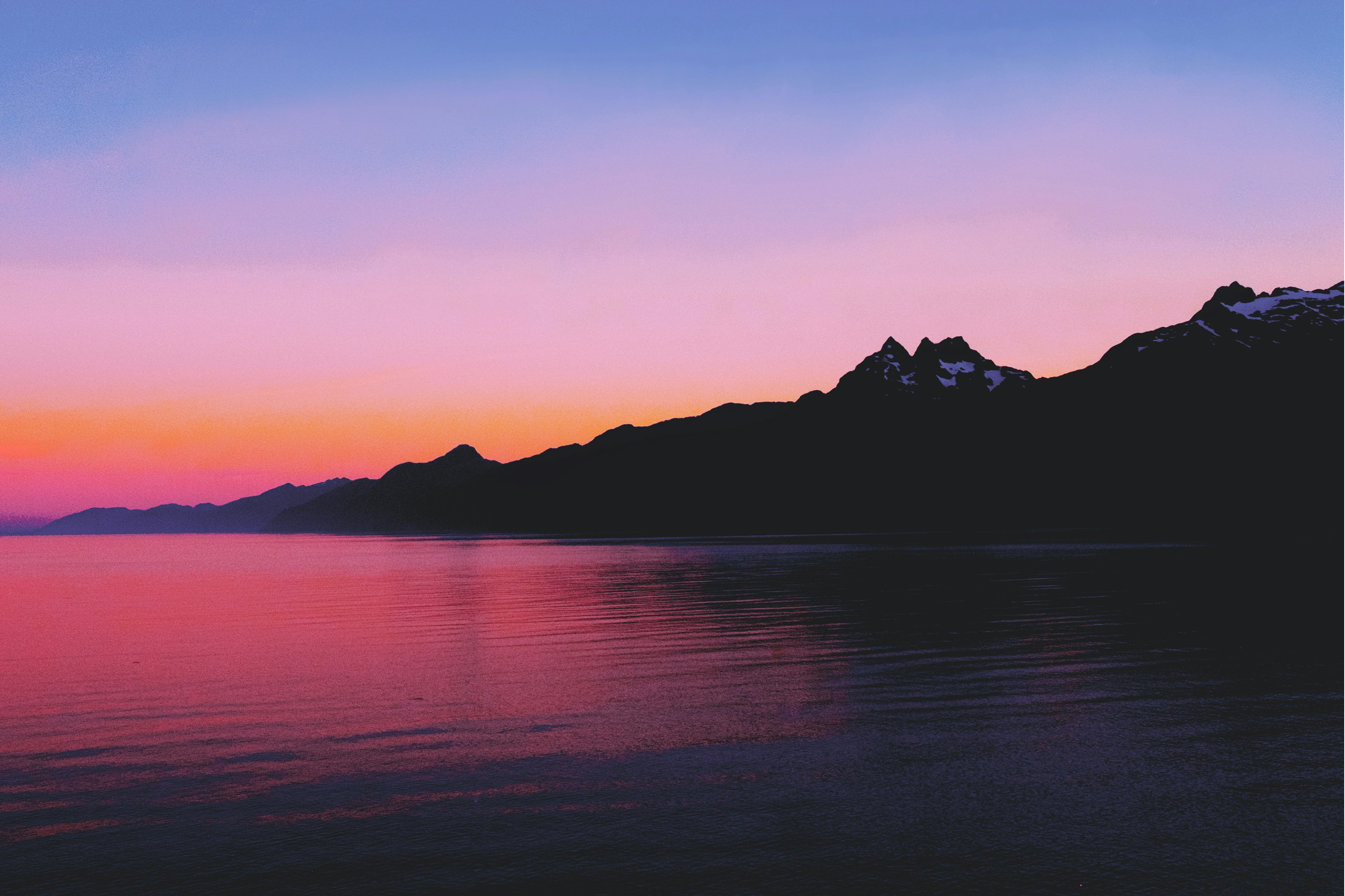 The sun sets behind a range of mountains, the lake is calm and still, and the sky is a dreamy palette of colors. - free wallpaper image