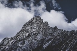 The top of the mountain is covered by clouds, the rock surface is grey and white - free wallpaper image