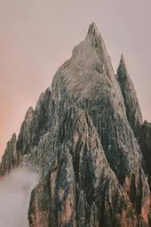 A towering mountain peak stands amidst a misty mountain range, the rock surface of the peak shows gray and pink, and the sky shows light pink. - free wallpaper image