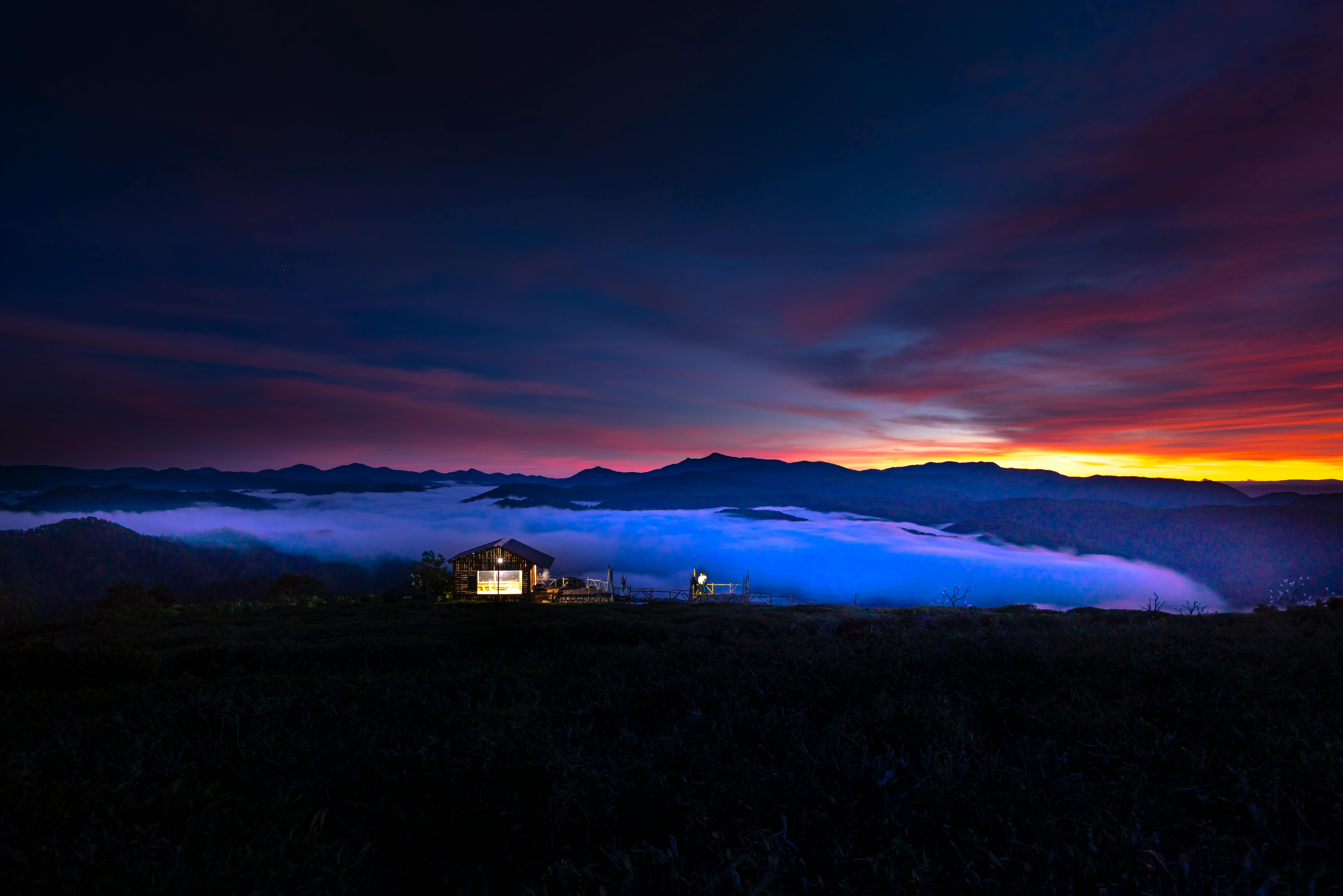 Rolling hills and sea of clouds, a small hut nestled in the mountains, with orange and red evening glow in the distance. - free wallpaper image