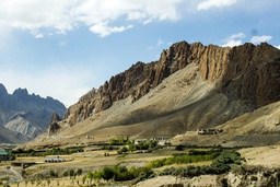 A mountain range with rugged peaks, the slopes are covered with sparse vegetation, and the distant sky is blue. - free wallpaper image