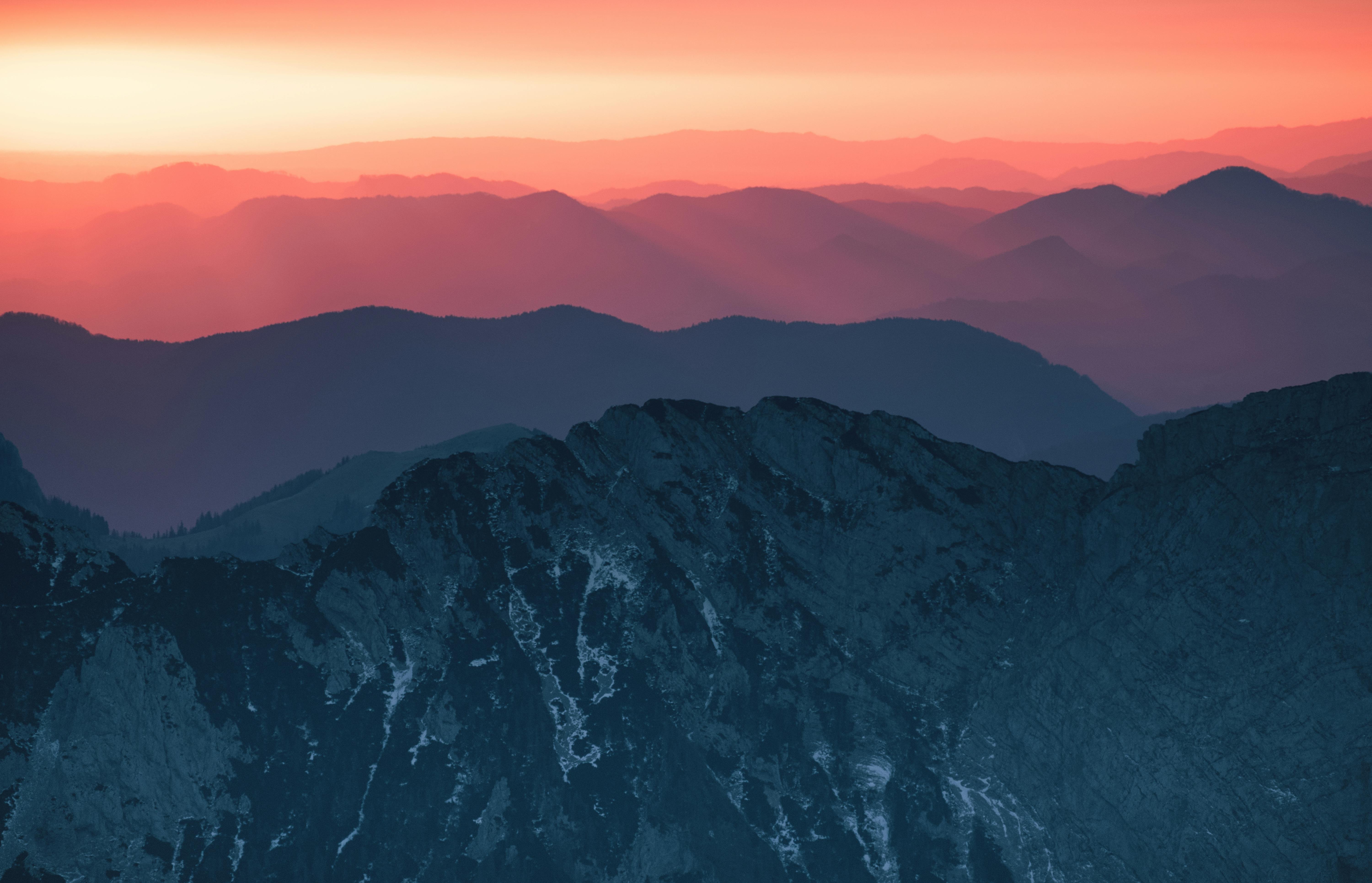 Layered mountains show a red hue under the glow of the setting sun. - free wallpaper image