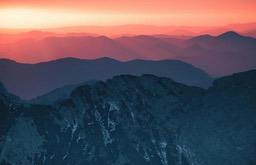 Layered mountains show a red hue under the glow of the setting sun. - free wallpaper image