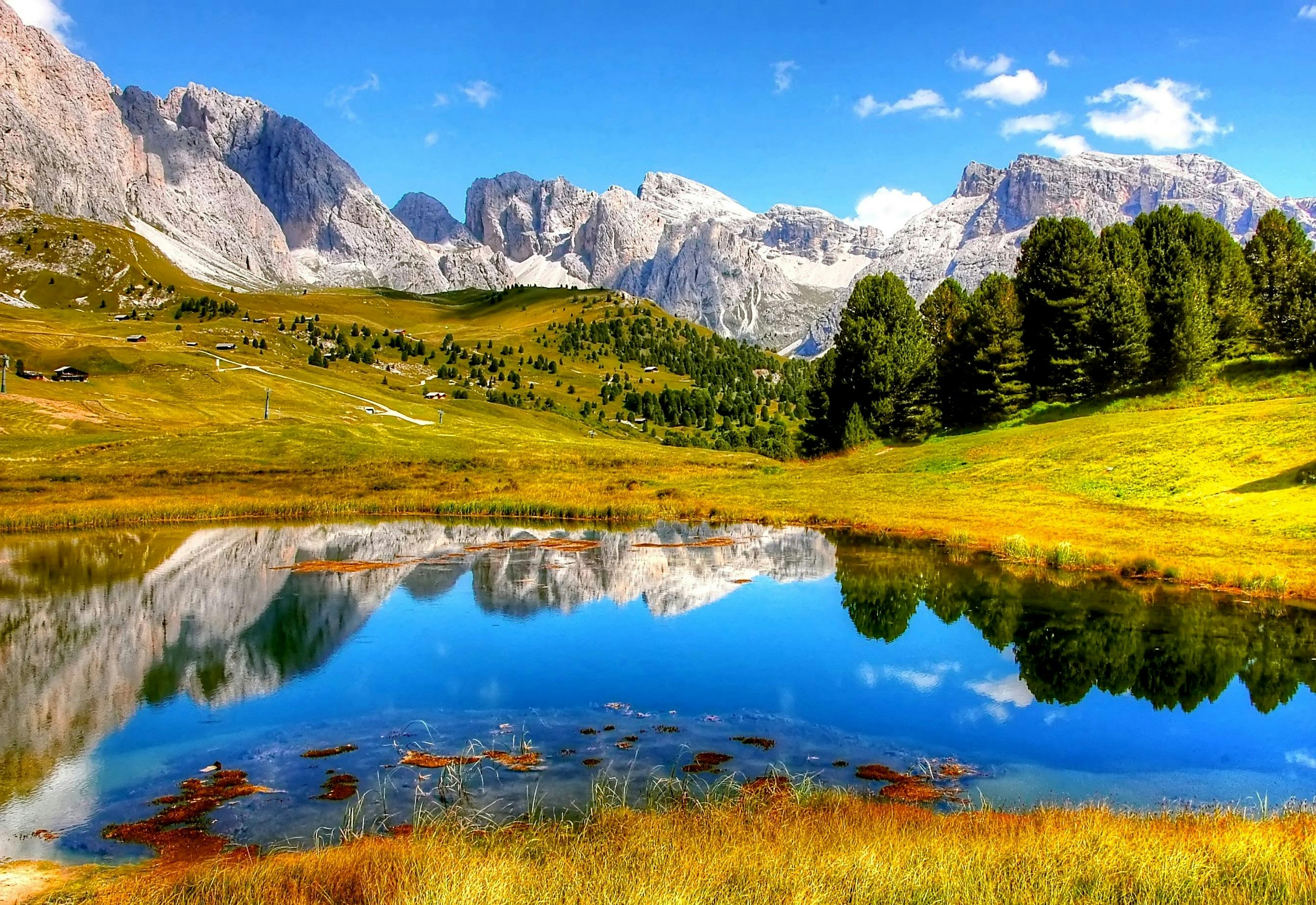 The mountain peaks are reflected in the clear lake, surrounded by green grass, blue sky and white clouds, the scenery is beautiful. - free wallpaper image