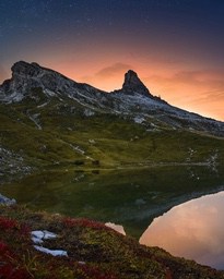 A mountain peak is reflected in the still waters of a lake, the sky is a mesmerizing orange-red, like the scene of a sunrise or sunset. - free wallpaper image