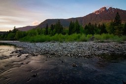 A river in the mountains at sunset, the riverbank is covered with pebbles, and the distant mountain peaks are covered with snow. - free wallpaper image