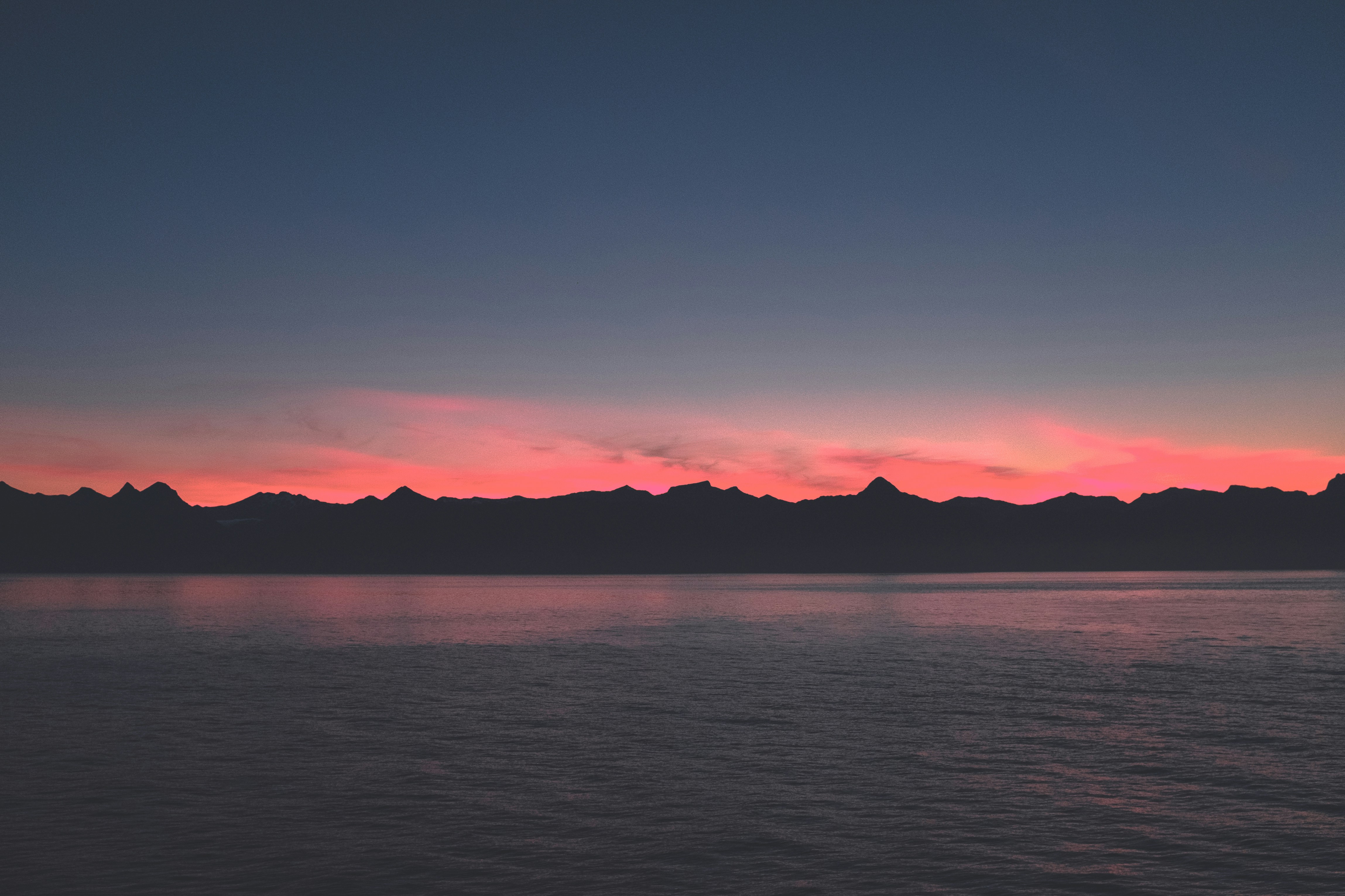 The silhouette of mountains against a pink sky at dusk, the calm sea reflects the afterglow. - free wallpaper image