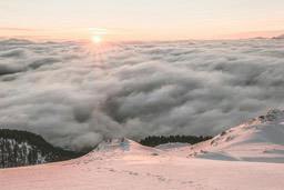 An aerial view of a sea of clouds, with an orange sun in the distance. - free wallpaper image