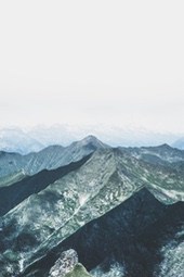 The mountains stretch as far as the eye can see, the peaks are particularly majestic against the backdrop of white clouds, and the distant sky is a pale blue. - free wallpaper image