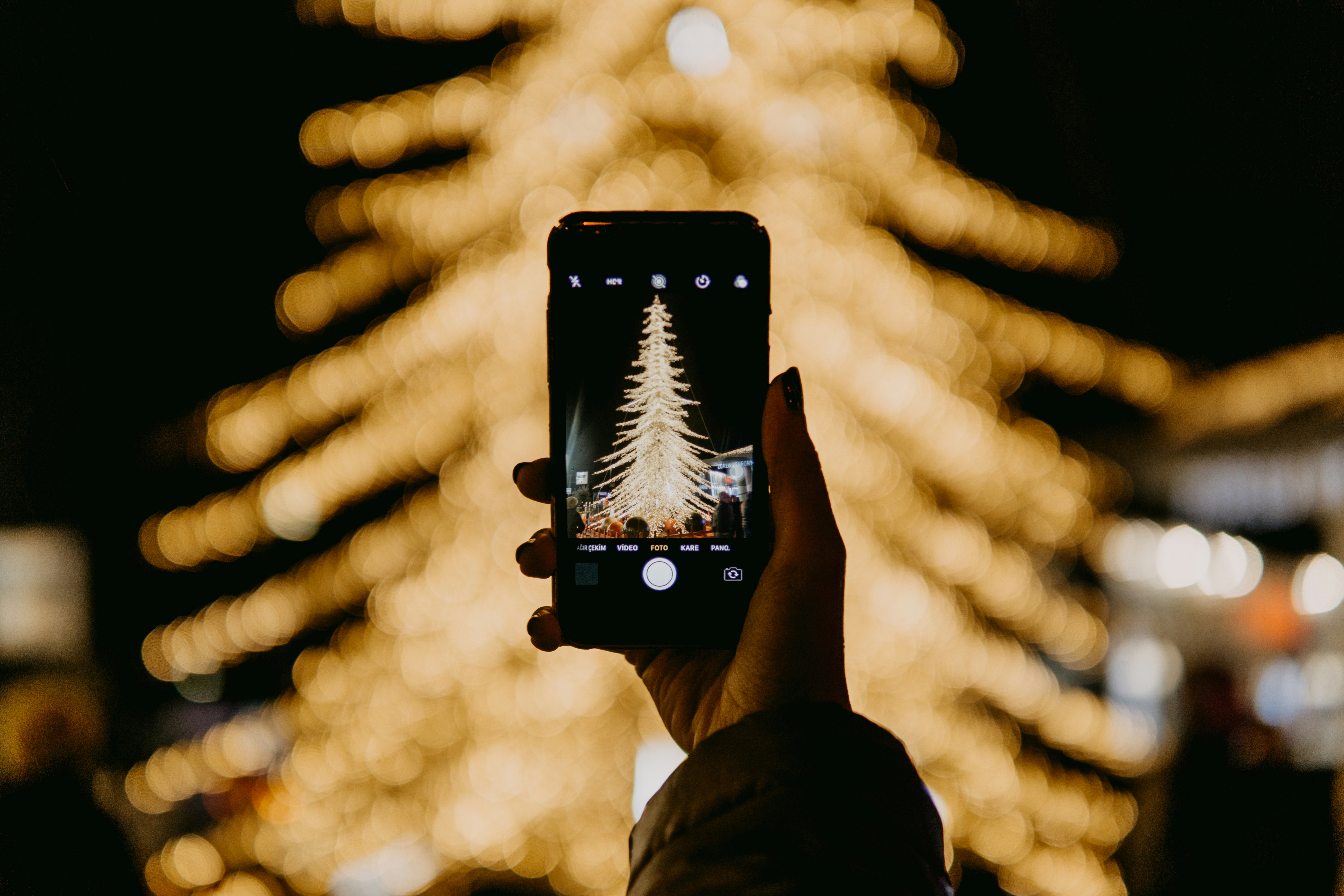 Someone is taking a photo of a Christmas tree decorated with colorful lights at night. - wallpaper image