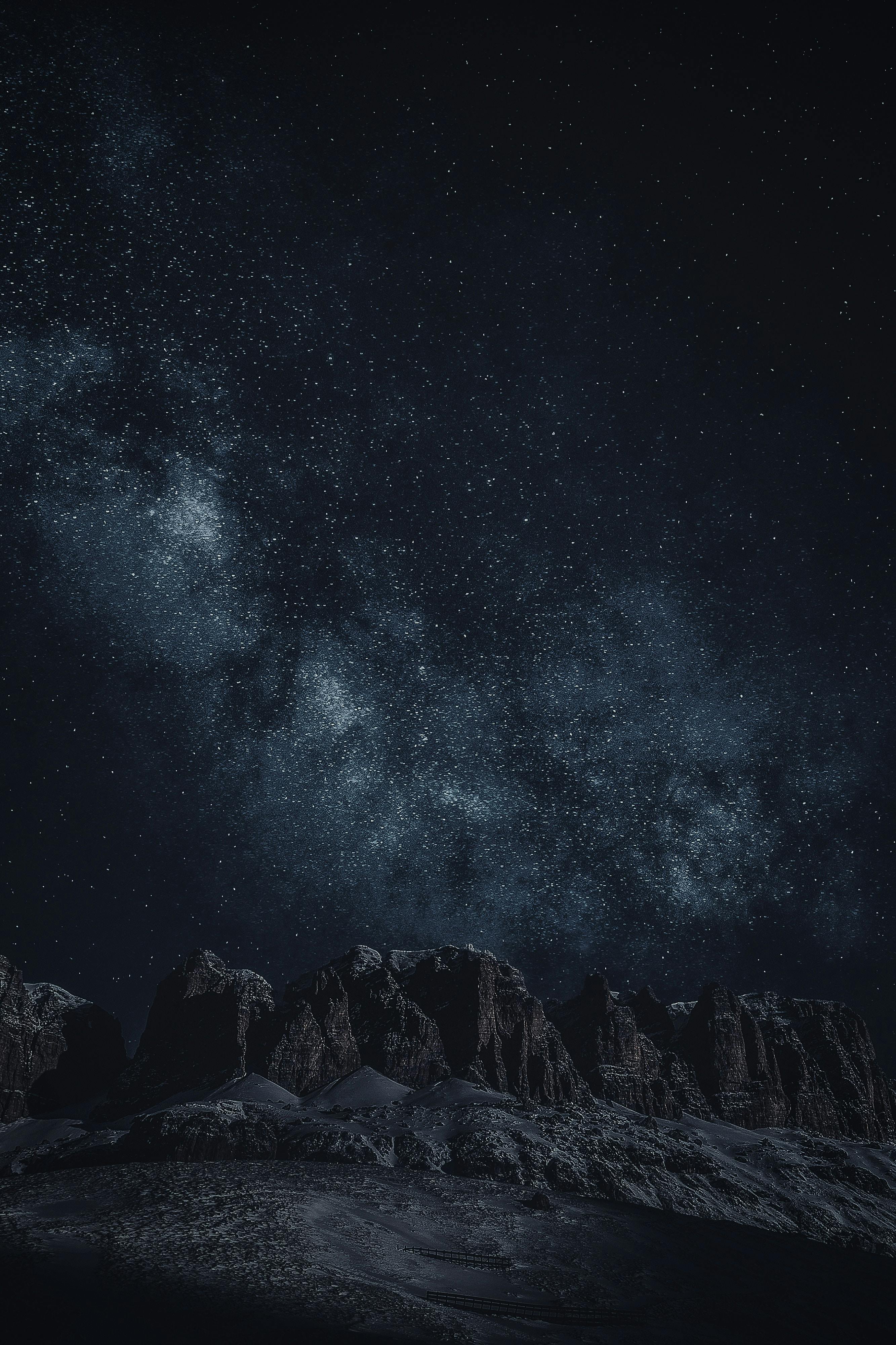 The night sky is dotted with stars, the Milky Way stretches across the sky, and mountains stand tall in the darkness. - free wallpaper image