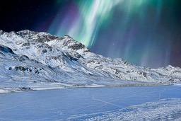 The aurora borealis shines in the night sky, illuminating the snow-covered mountains and frozen lake. - free wallpaper image