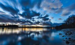 A peaceful lake reflects the colors of the sky at dusk, with distant trees blending with the clouds to create a beautiful scene. - free wallpaper image