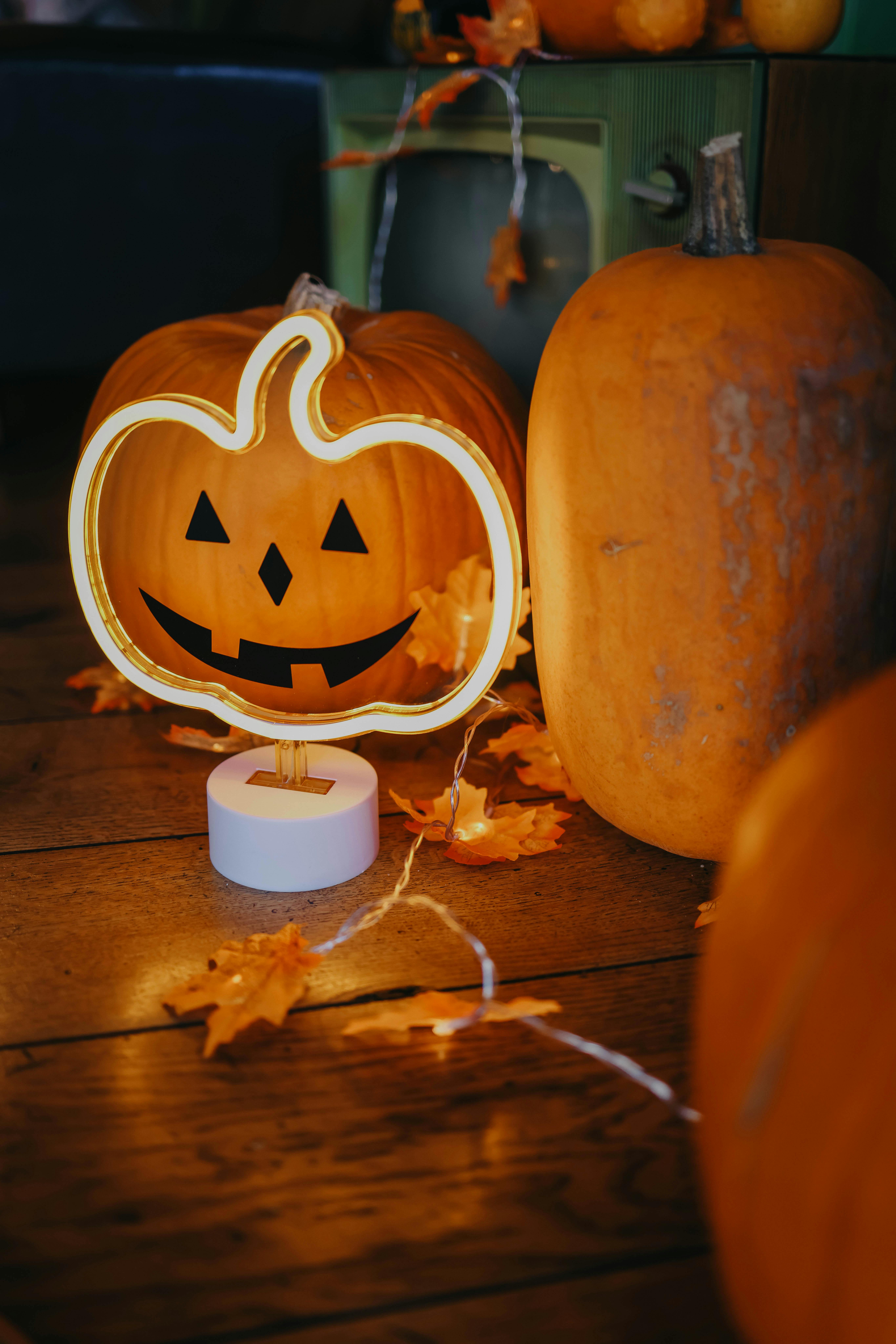 Three pumpkins are placed on a wooden table, one of which is a lit pumpkin lamp, with some dry leaves scattered around. - wallpaper image