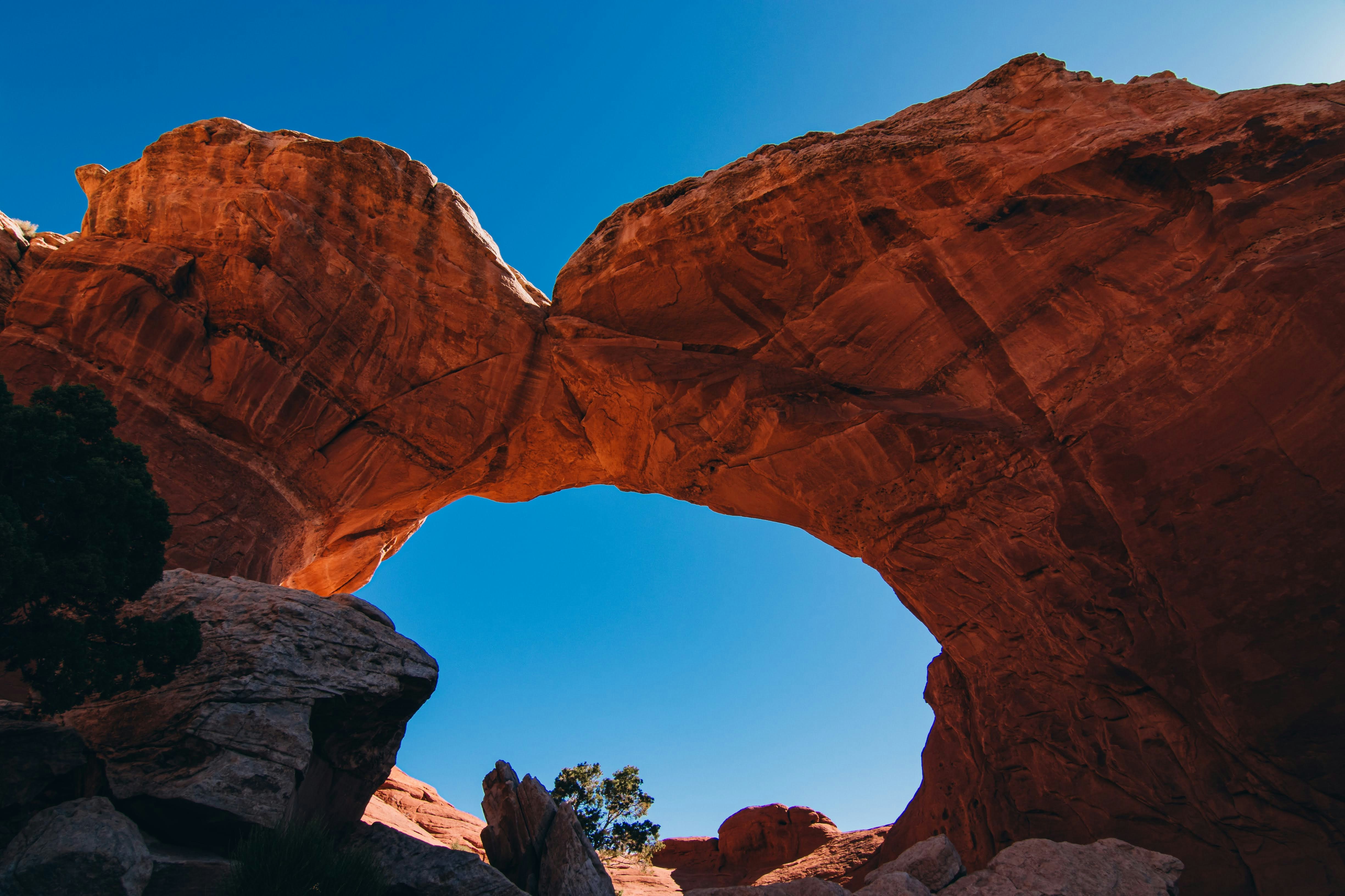 A red arched rock viewed from below, with a blue sky as background. - free wallpaper image