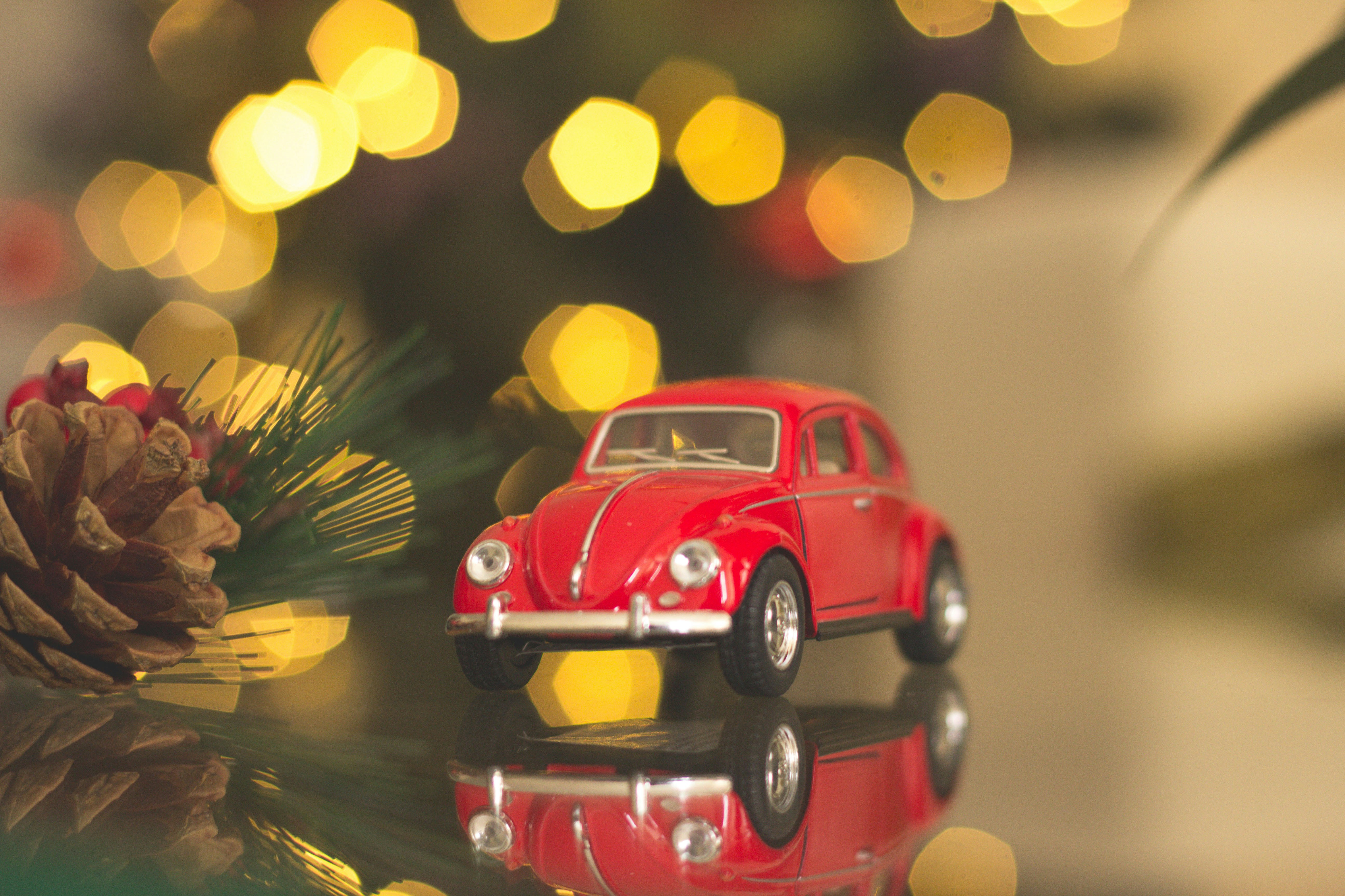 A red toy Volkswagen Beetle car placed next to a Christmas tree, with gold lights and green branches in the background, creating a festive atmosphere. - wallpaper image