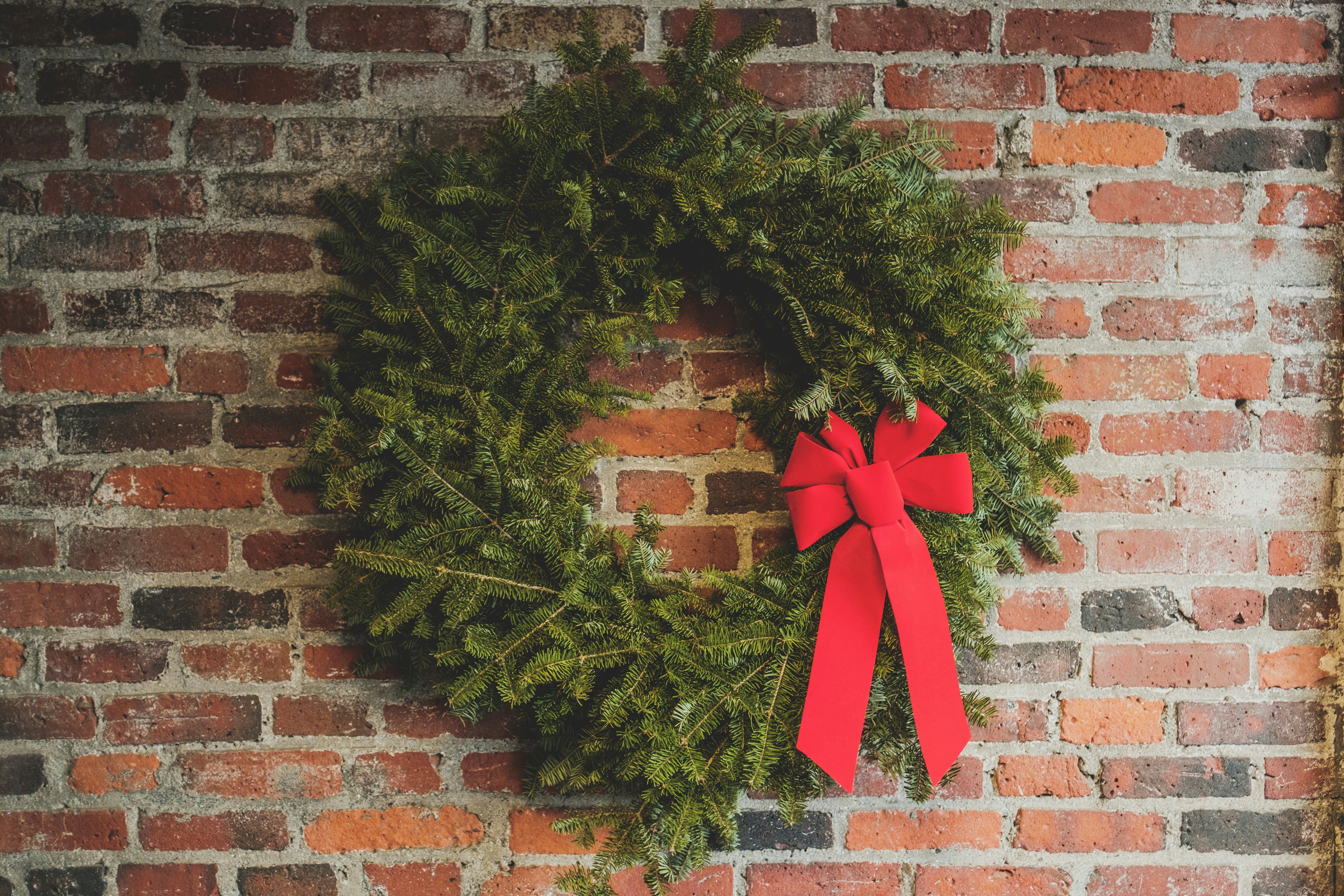 A red Christmas wreath decorates a red brick wall. - wallpaper image