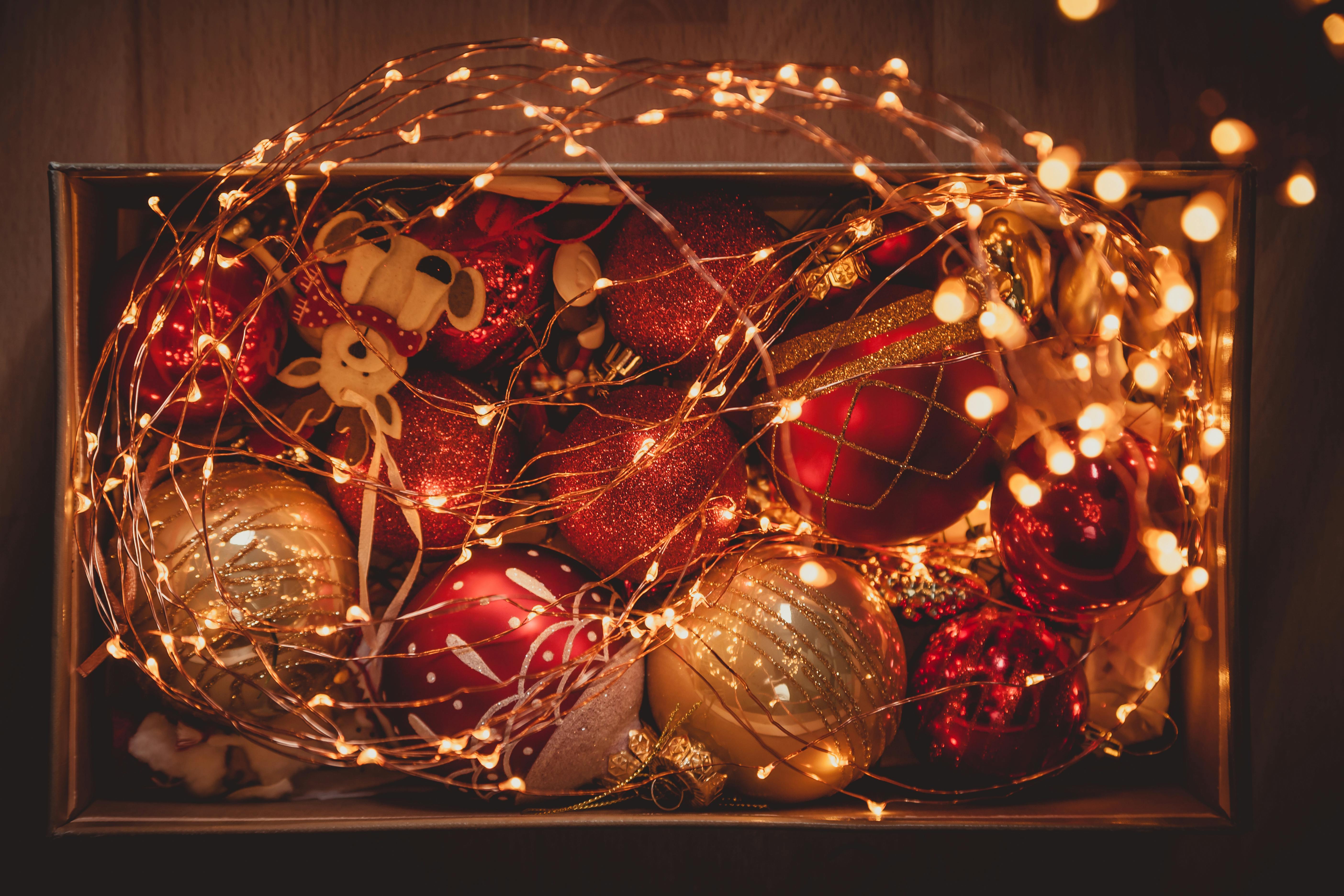 A wooden box filled with red and gold Christmas balls, surrounded by warm yellow string lights. - wallpaper image