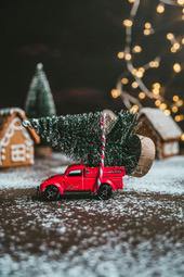 A red toy truck is carrying a Christmas tree, next to gingerbread houses, on a white snowy ground. - wallpaper image