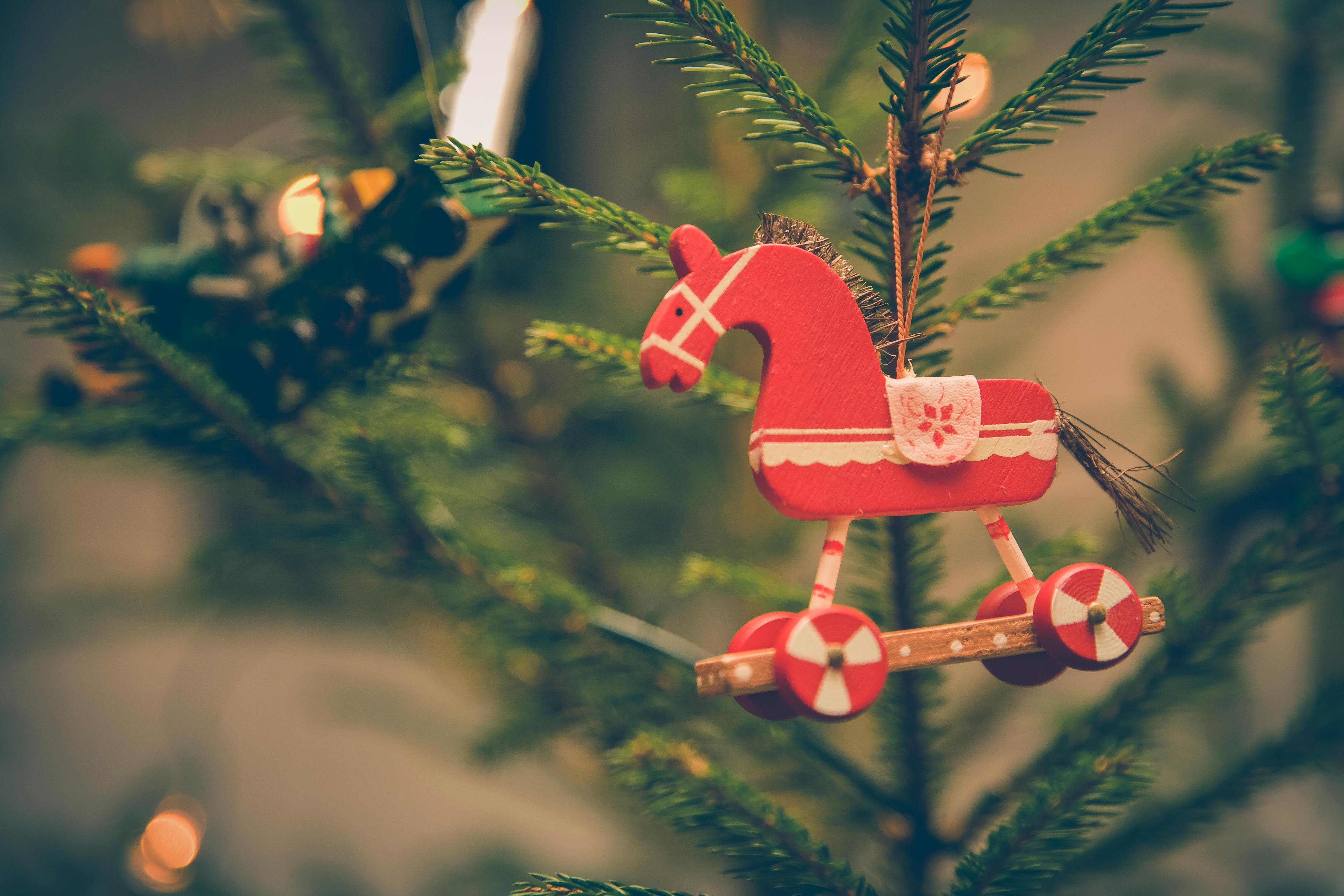 A red wooden rocking horse ornament hangs on a Christmas tree - wallpaper image