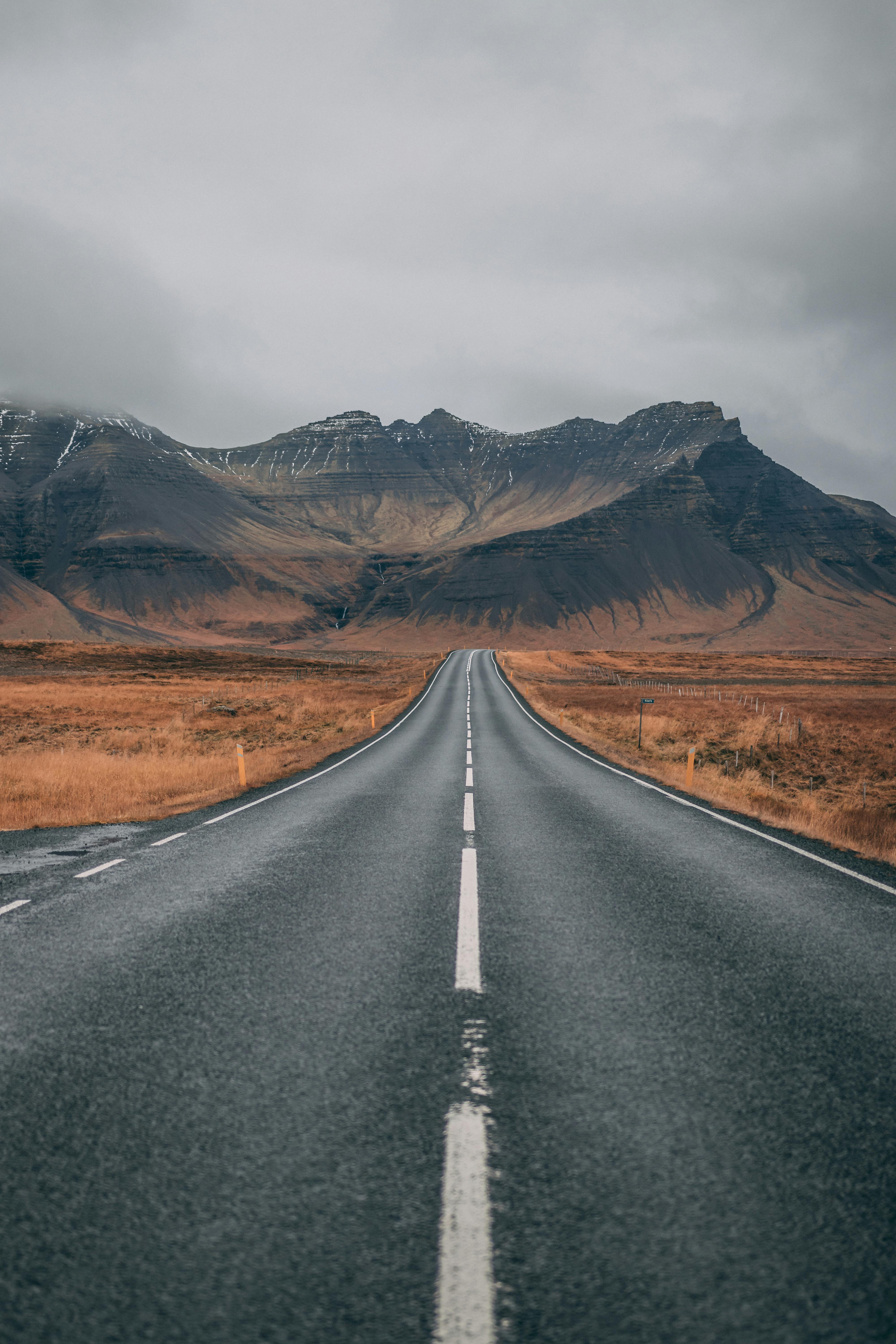 A straight road leading to the mountains in the distance, the road is flanked by desolate land. - free wallpaper image