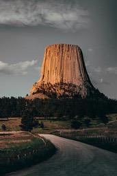 A massive rock formation stands tall on a vast field of grass, with a winding road leading up to it in the distance. - free wallpaper image