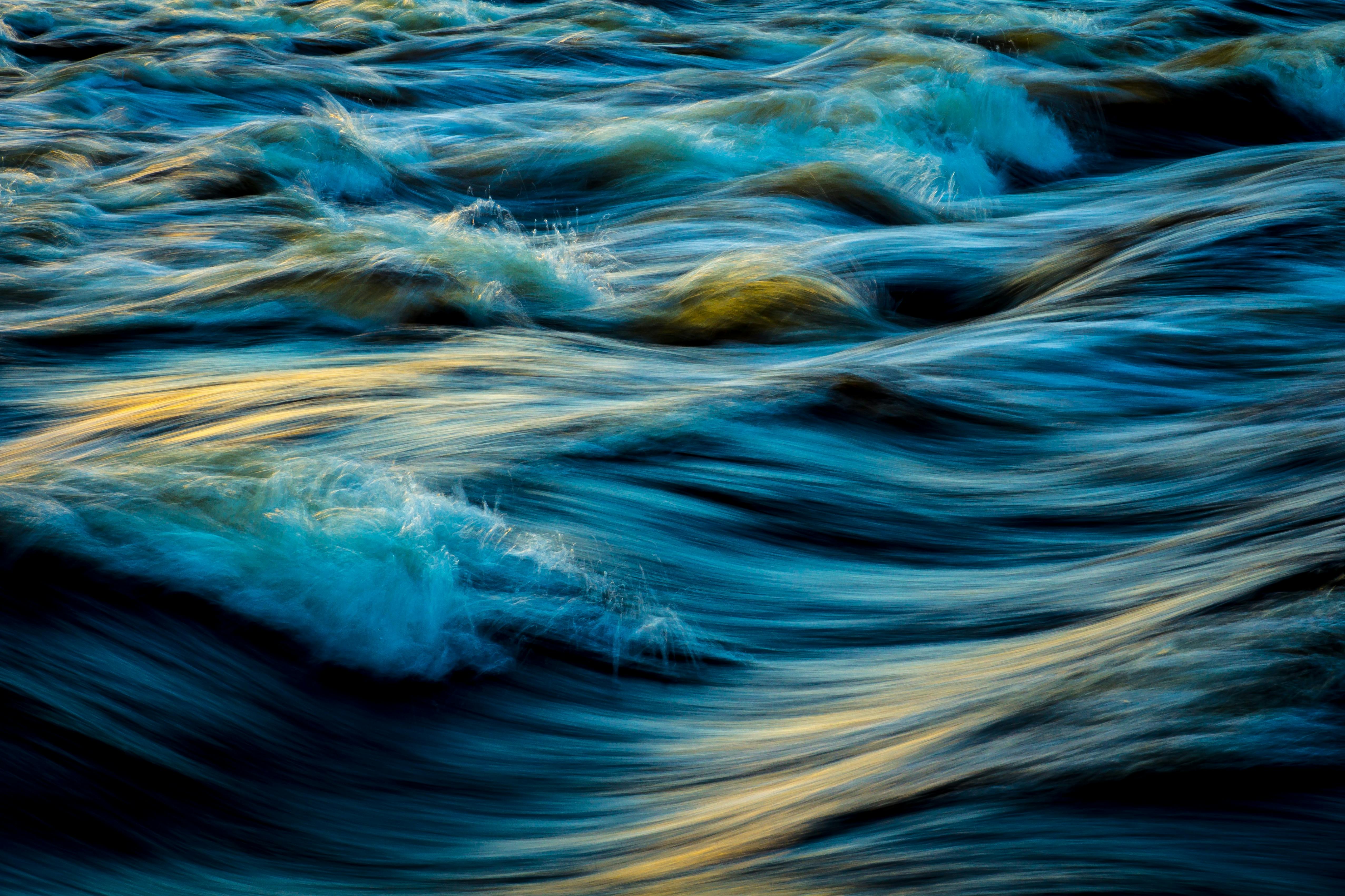 Rushing water creates waves, with golden light reflecting off the surface, showcasing the flow and power of water. - free wallpaper image