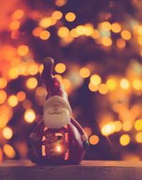 A Santa Claus candle decoration is placed on a wooden table, with a warm-toned light background - wallpaper image