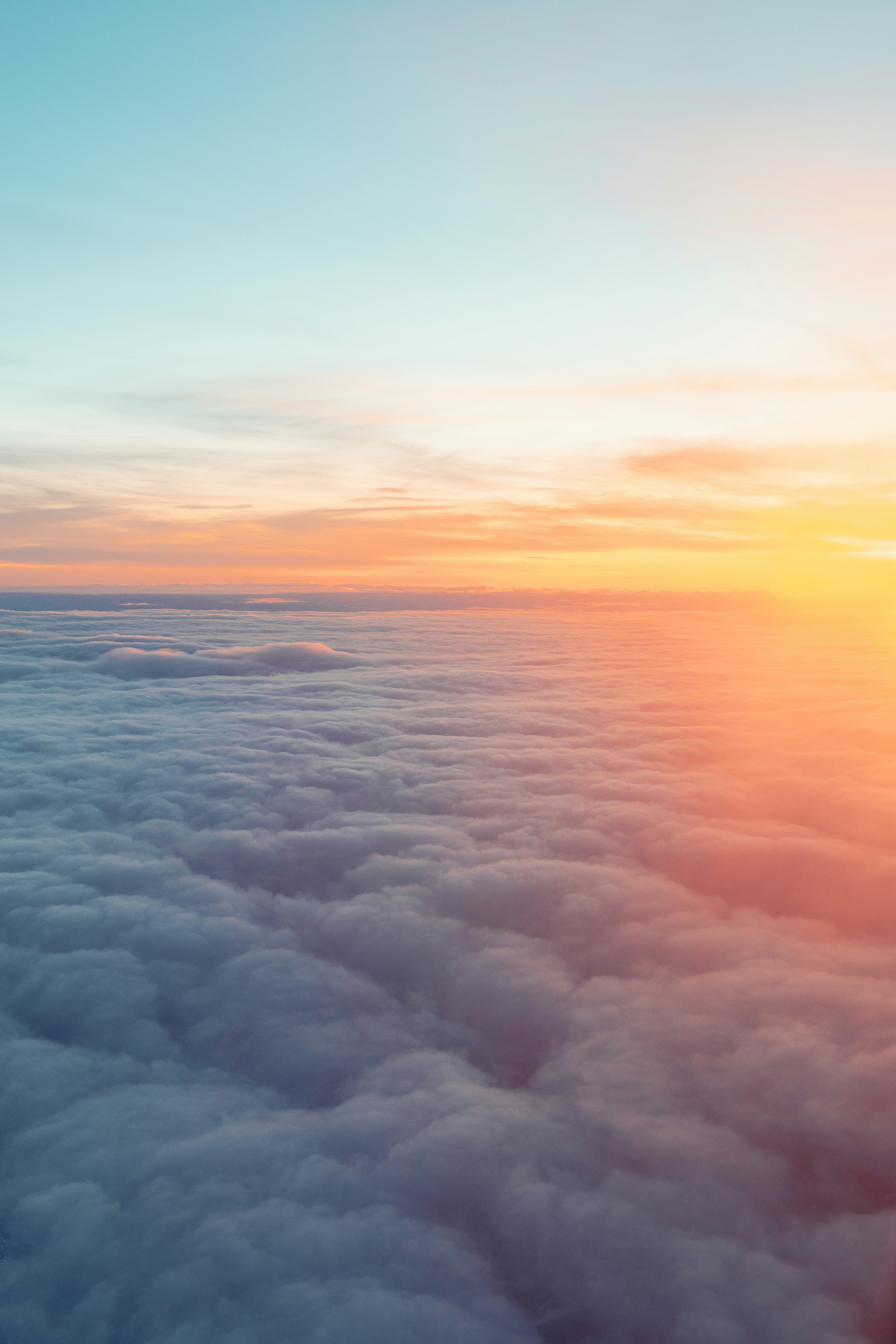 An aerial view of a sea of clouds, the sky is tinged with orange and pink, the clouds are undulating like waves, the scene is spectacular. - free wallpaper image