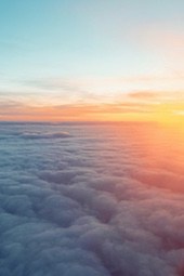 An aerial view of a sea of clouds, the sky is tinged with orange and pink, the clouds are undulating like waves, the scene is spectacular. - free wallpaper image