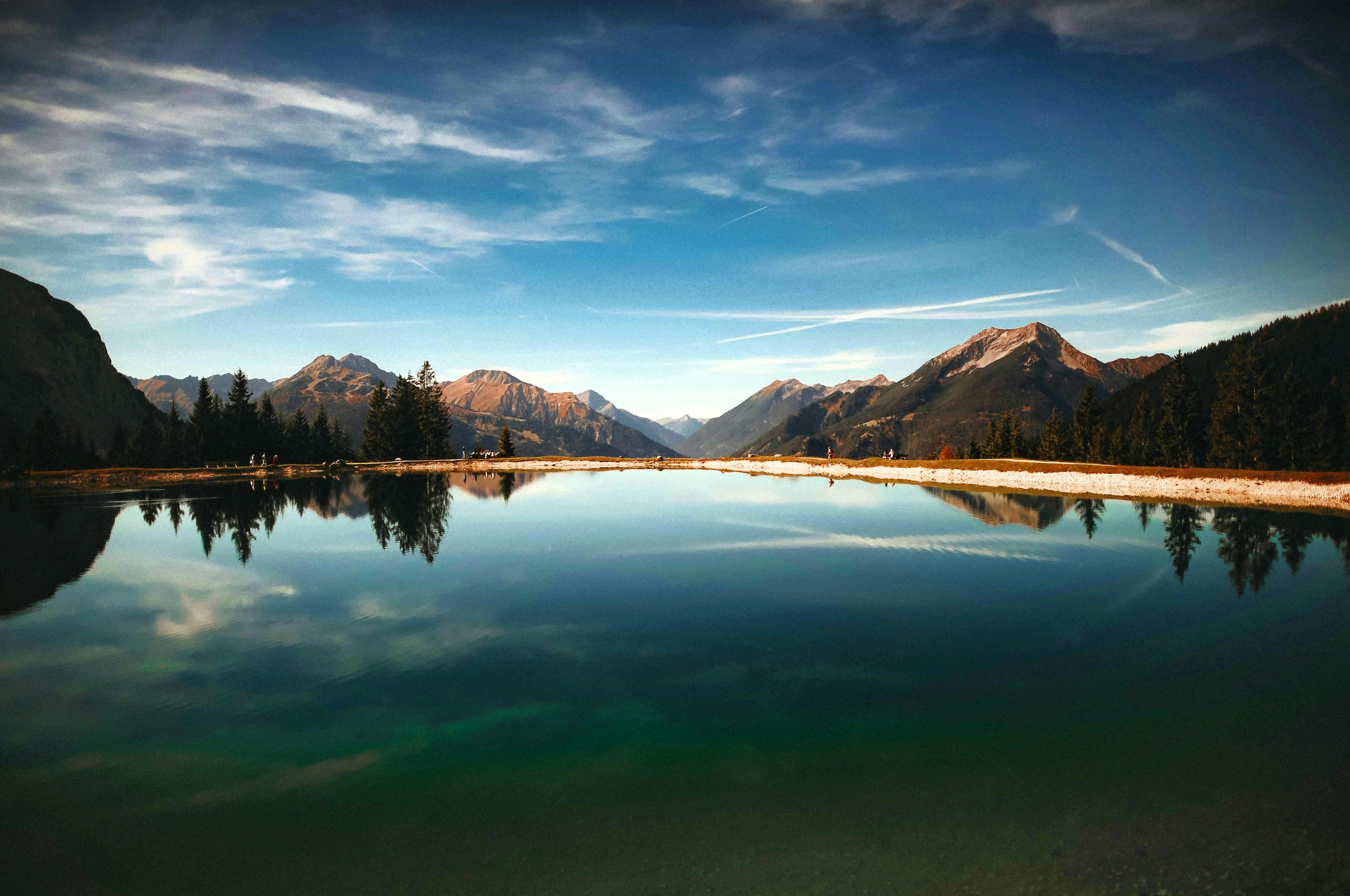 A serene lake reflects the blue sky, white clouds, and distant mountains, creating a beautiful natural landscape. - free wallpaper image