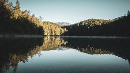 A serene lake reflecting the blue sky and white clouds, with distant mountains covered by green forests, the scene is peaceful and beautiful. - free wallpaper image