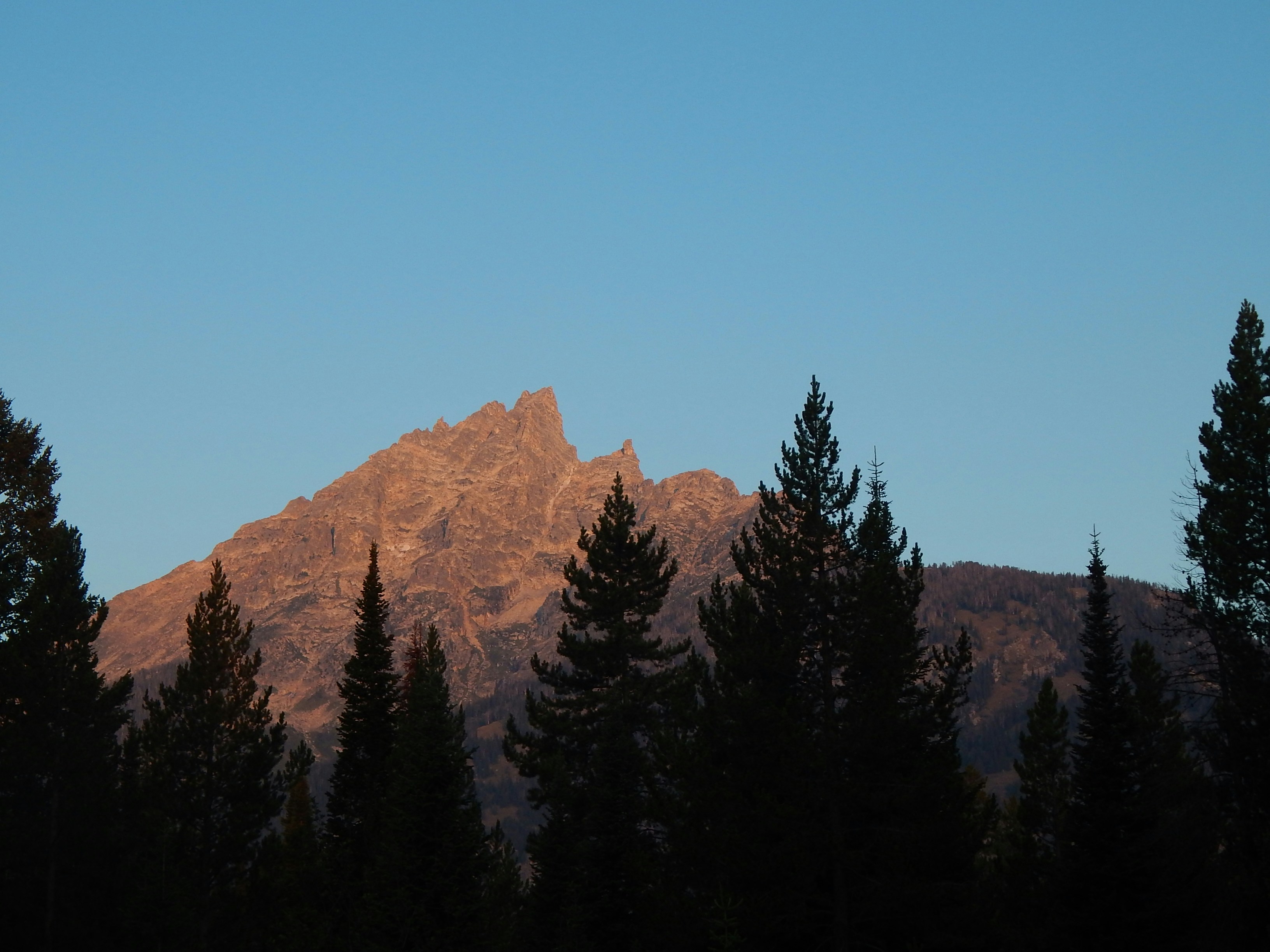 The mountain peaks are a warm orange in the setting sun, and the trees around the peaks are silhouetted in the evening glow. - free wallpaper image