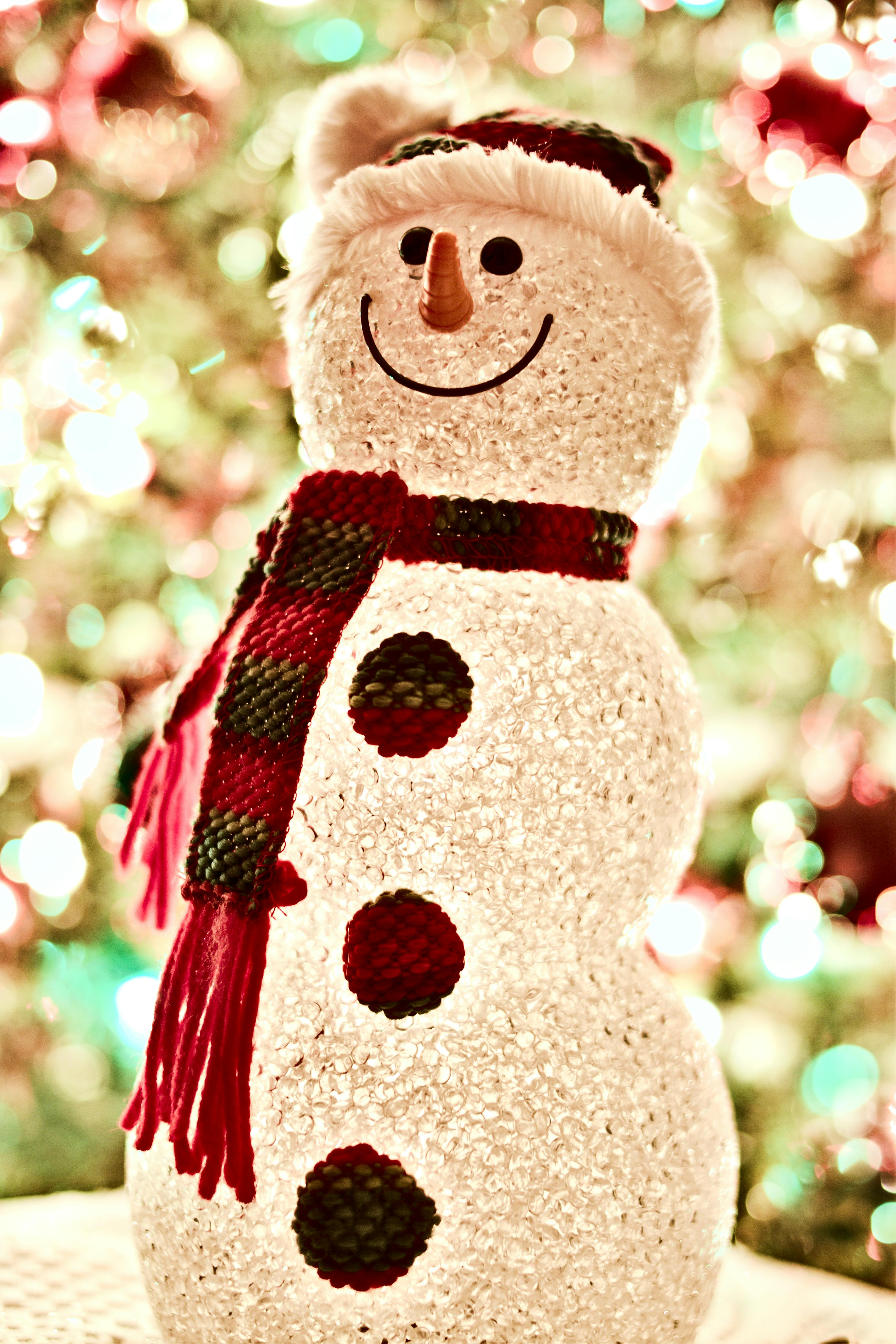 A smiling snowman stands in front of a Christmas tree with twinkling lights. - wallpaper image