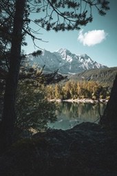 A snow-capped mountain in the distance is reflected in the calm lake water. Trees surround the lake, and the scene is peaceful and tranquil. - free wallpaper image