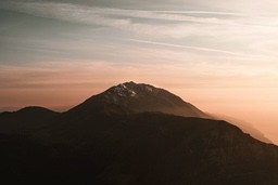 A mountain range with snow-capped peaks is bathed in the orange glow of the setting sun. - free wallpaper image