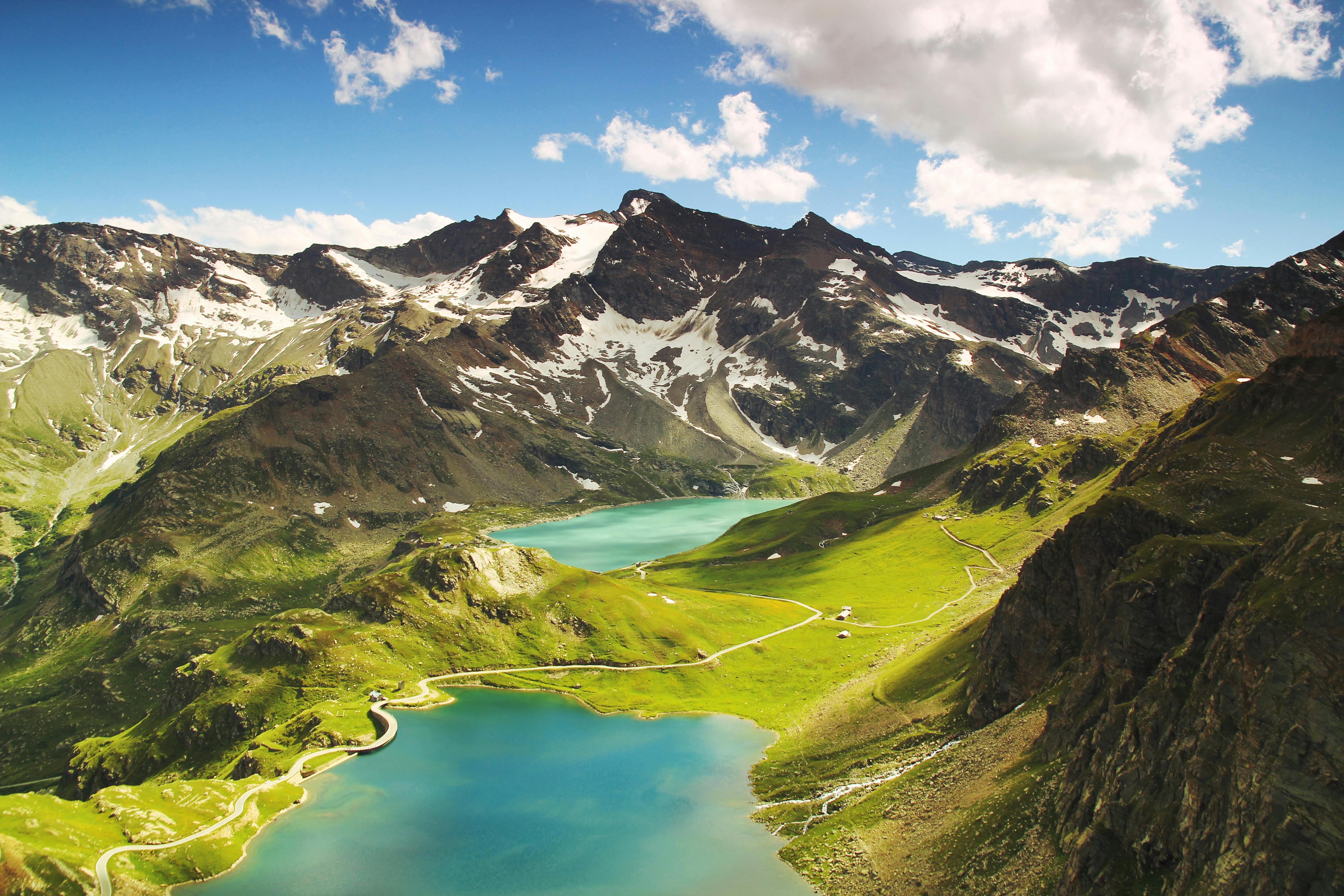 Two turquoise lakes are nestled between towering mountains, the peaks are covered with snow, the sky is clear and white clouds are floating. - free wallpaper image