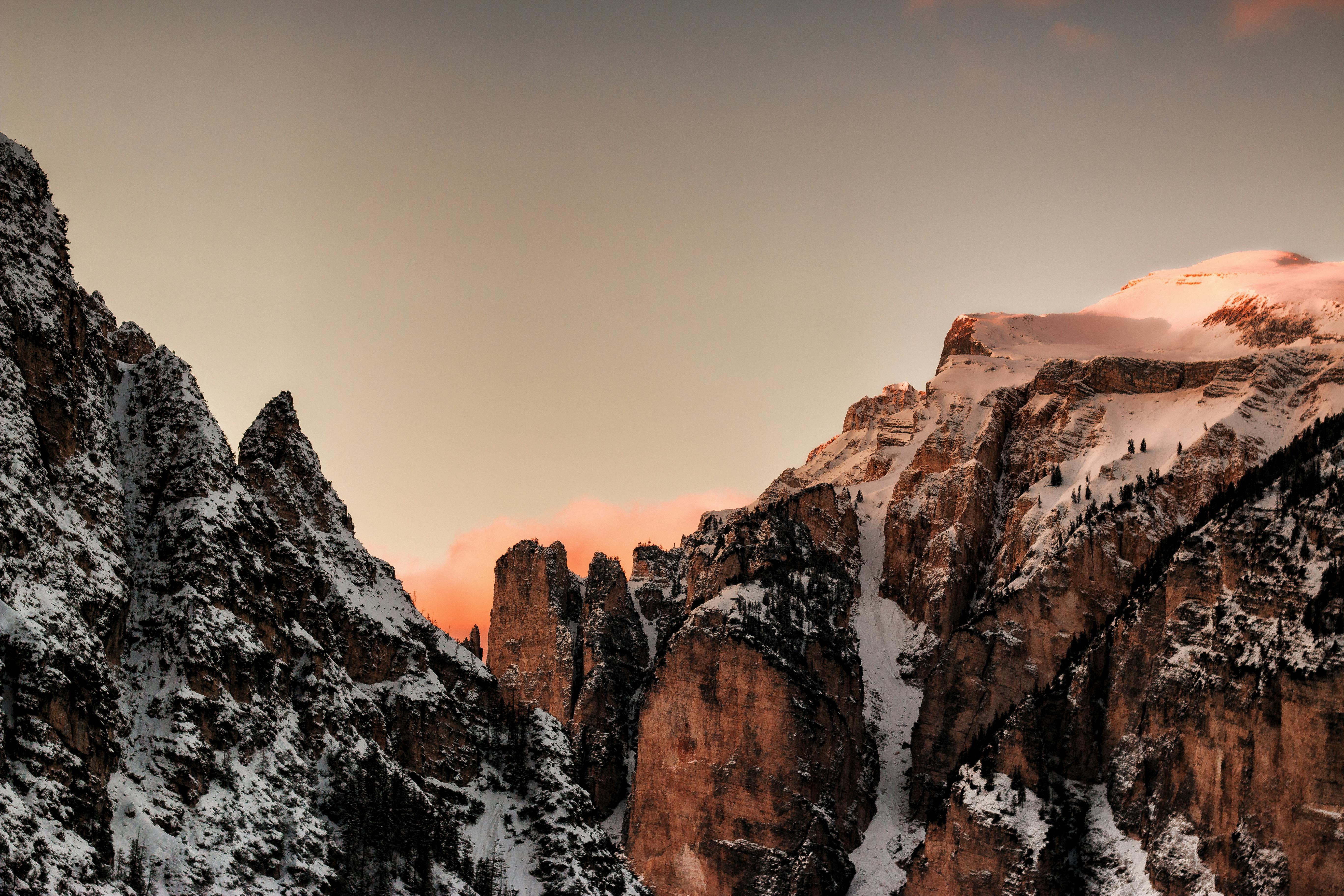 Sunlight bathes snow-covered mountain peaks at dusk, forming a narrow valley between them. - free wallpaper image