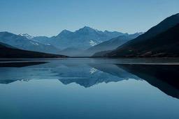 A tranquil lake reflects the distant snow-capped mountains, the sky is azure blue, presenting a serene natural landscape. - free wallpaper image