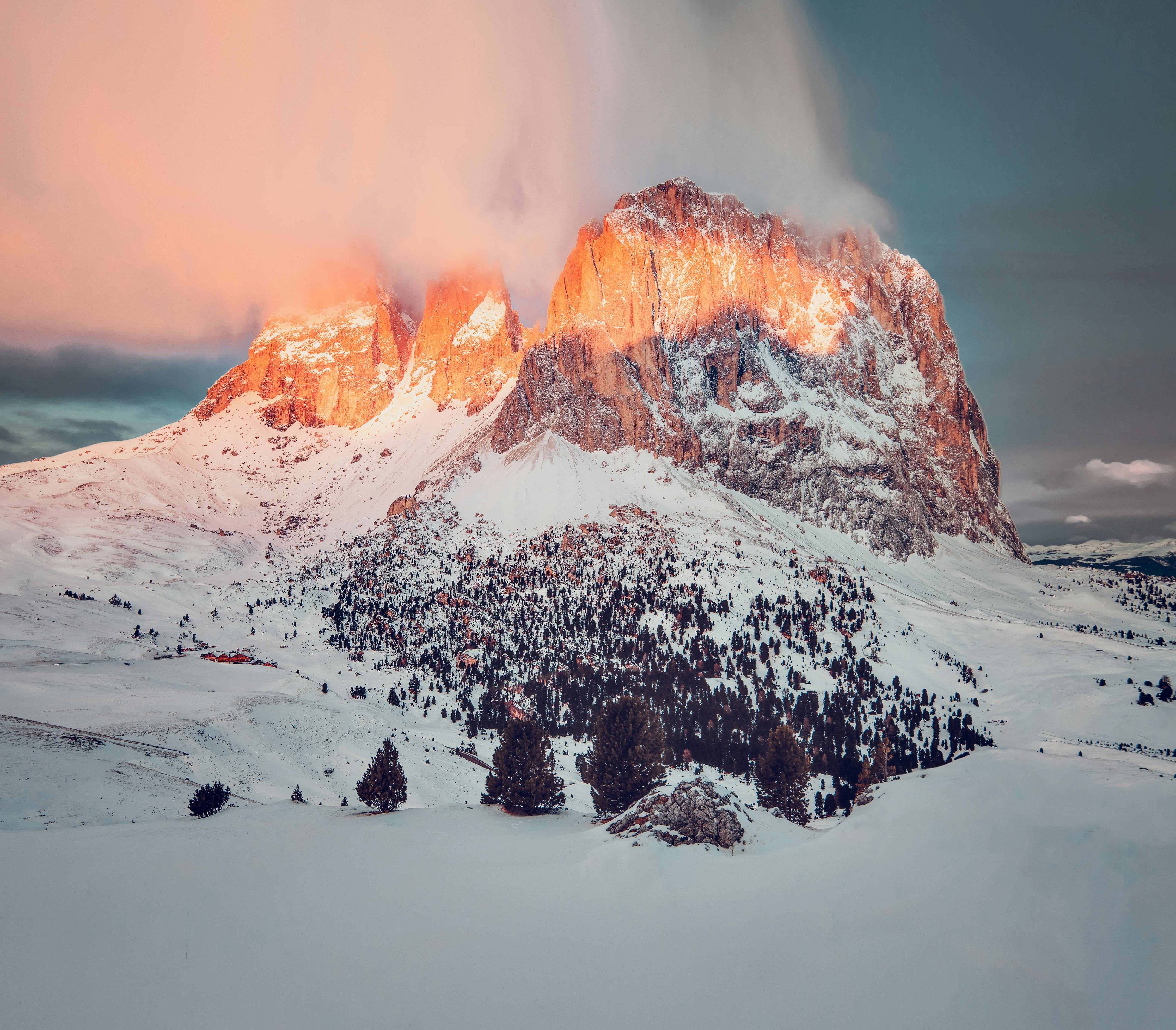 A massive snow mountain bathed in warm sunlight at sunrise, the peak is painted in golden red, clouds drift over the mountaintop, presenting a magnificent natural landscape. - free wallpaper image