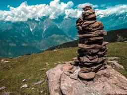 The mountains in the distance are covered with snow, the slopes are covered with green grass, and there are a few rocks in the foreground, one of which is piled with many stones to form a stone tower. - free wallpaper image