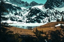 A lake surrounded by snow-capped mountains, the surface of the lake is calm, and the surroundings are covered with lush trees and grass. - free wallpaper image