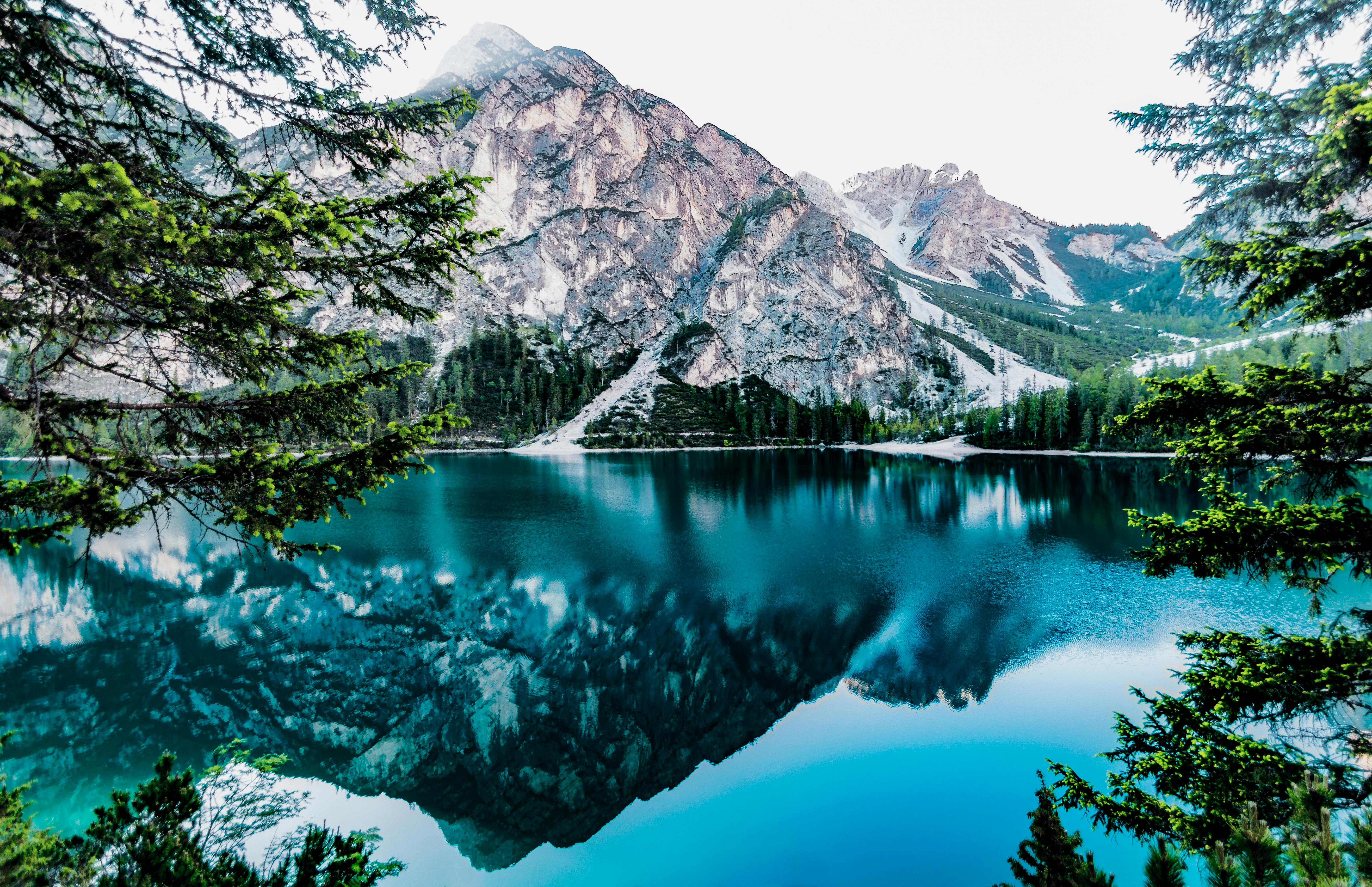 A serene lake reflects a majestic snowy mountain, the water is clear and blue, surrounded by lush forests, the scenery is beautiful and peaceful. - free wallpaper image