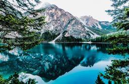 A serene lake reflects a majestic snowy mountain, the water is clear and blue, surrounded by lush forests, the scenery is beautiful and peaceful. - free wallpaper image