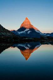 A mountain peak is reflected in a still lake. The sky is blue, the mountain is brown and the top of the mountain is covered with white snow. - free wallpaper image