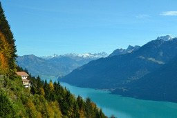 There is snow on the mountains in the distance, a blue river in the mountains, and houses and trees by the river. - free wallpaper image