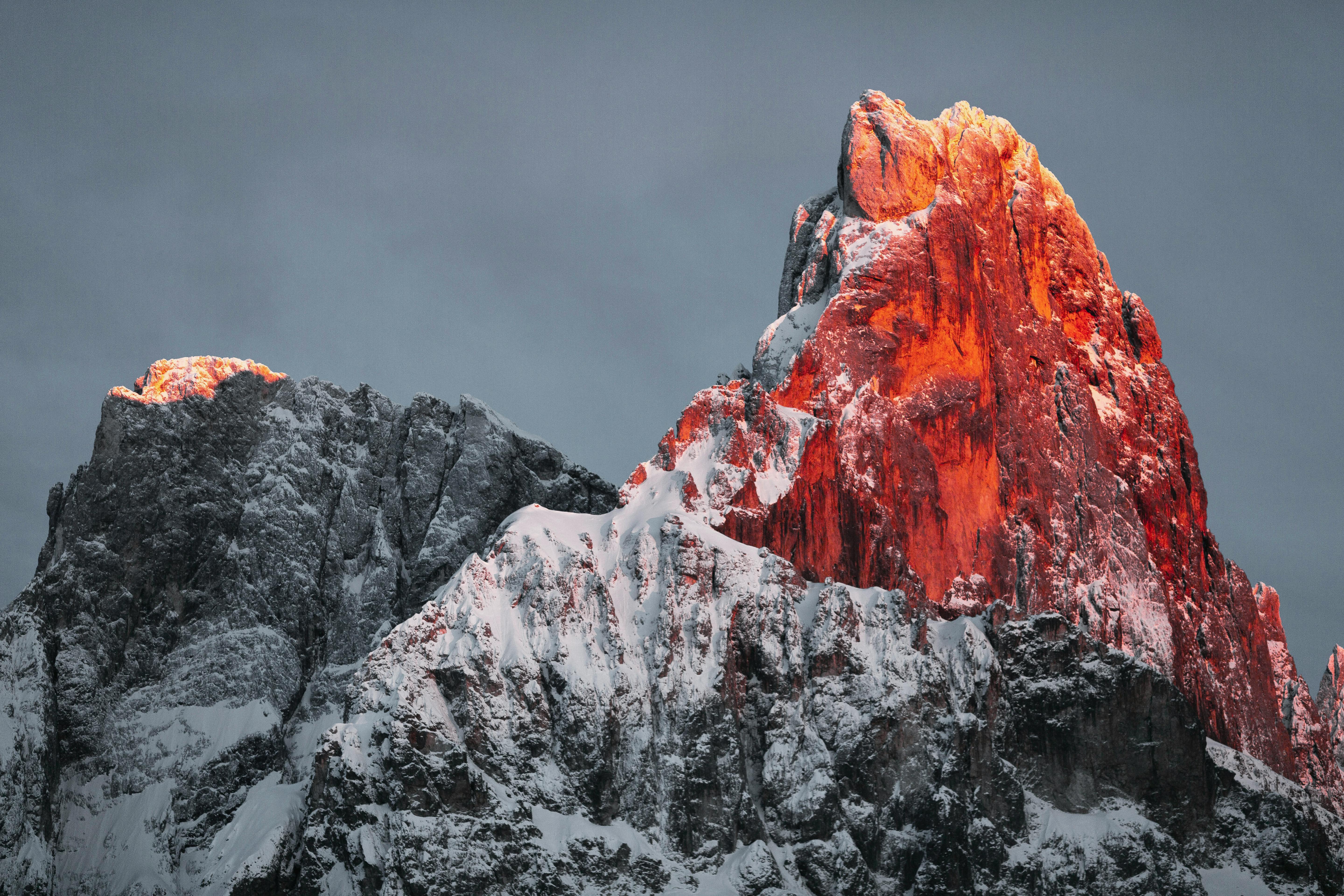 The setting sun shines on the peak of a snowy mountain, the peak is dyed red, the top is covered with snow, and the mountain is surrounded by gray clouds. - free wallpaper image