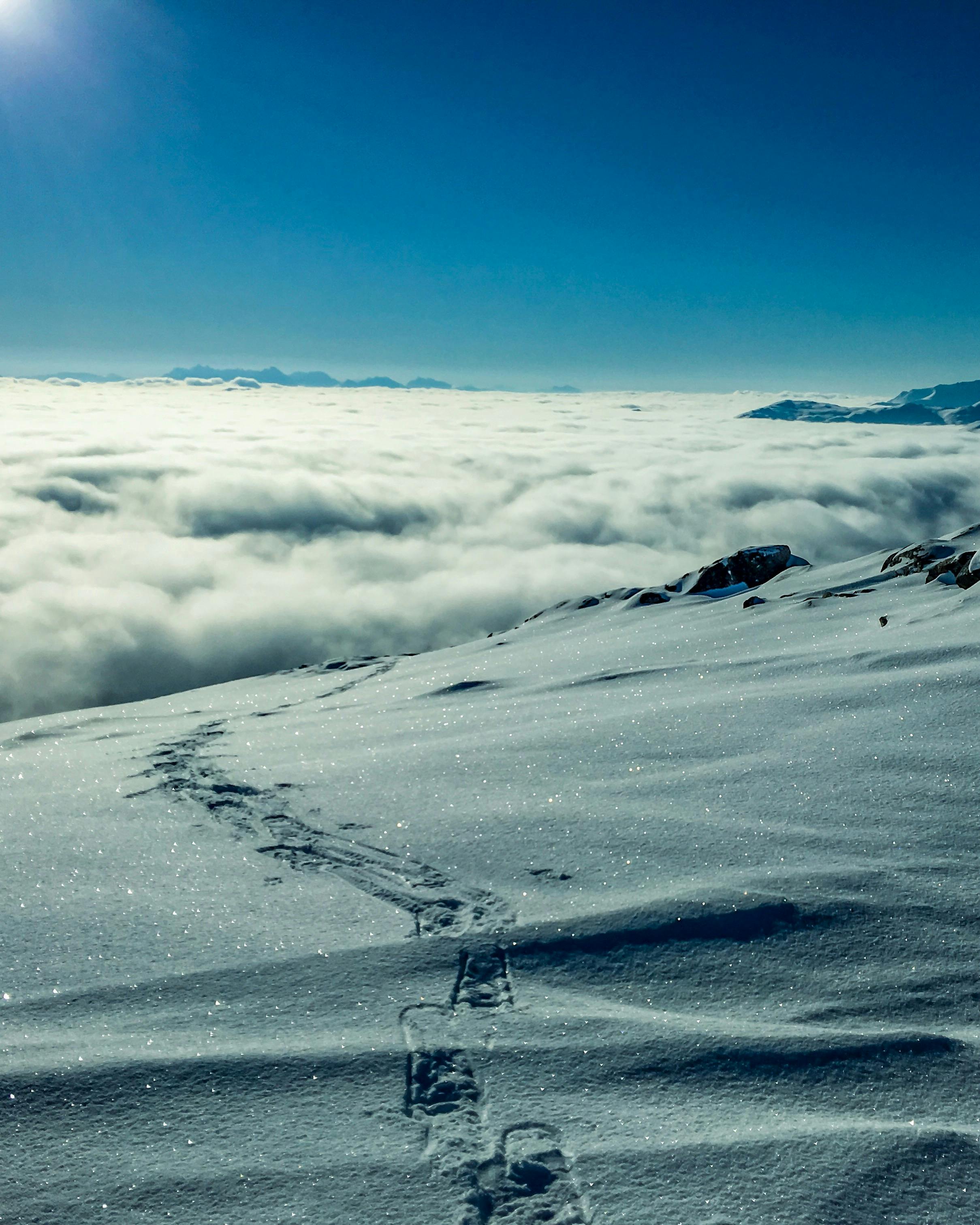 The mountain top is covered with white snow, the mountains in the distance are covered by a sea of clouds, and a trail of footprints is left on the snow. - free wallpaper image